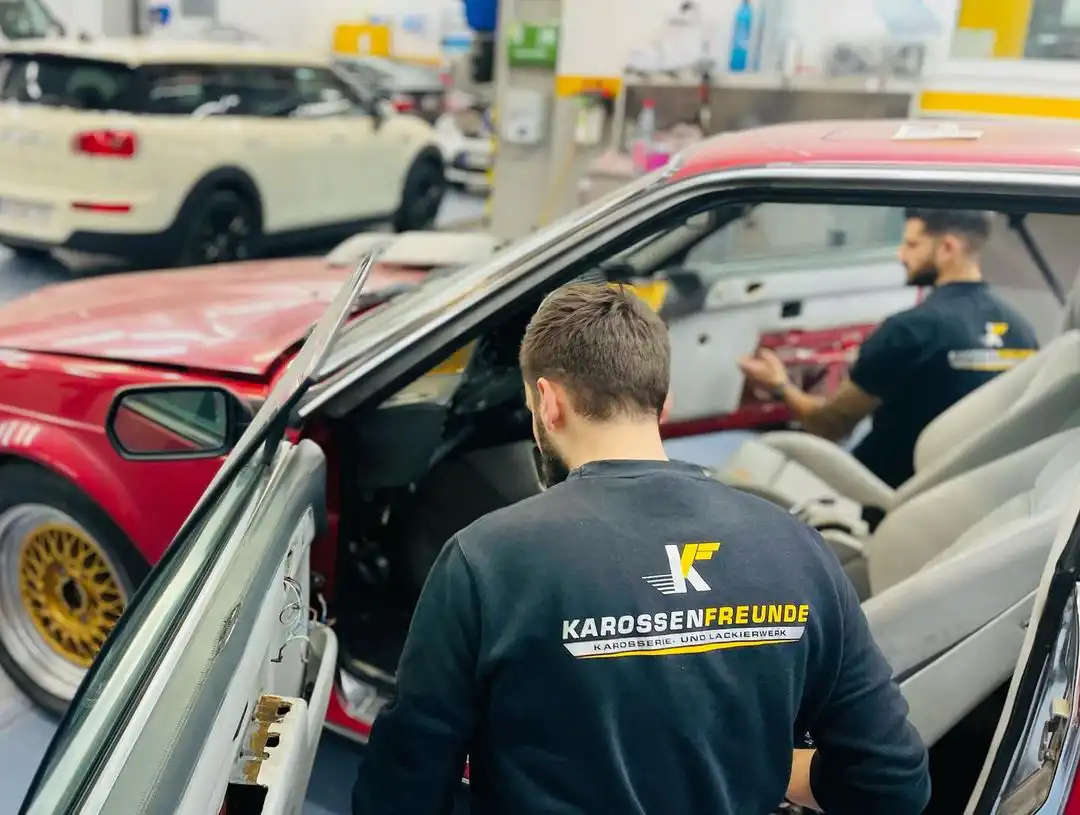 Die beiden Inhaber der Karossenfreunde, die Pullis mit dem Logo der Karossenfreunde tragen, bei der Arbeit an einem Auto.